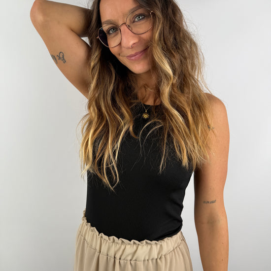 Frau mit schwarzem Ripp-Top und beigem Volant-Rock – natürlicher Look mit eleganter Schlichtheit.