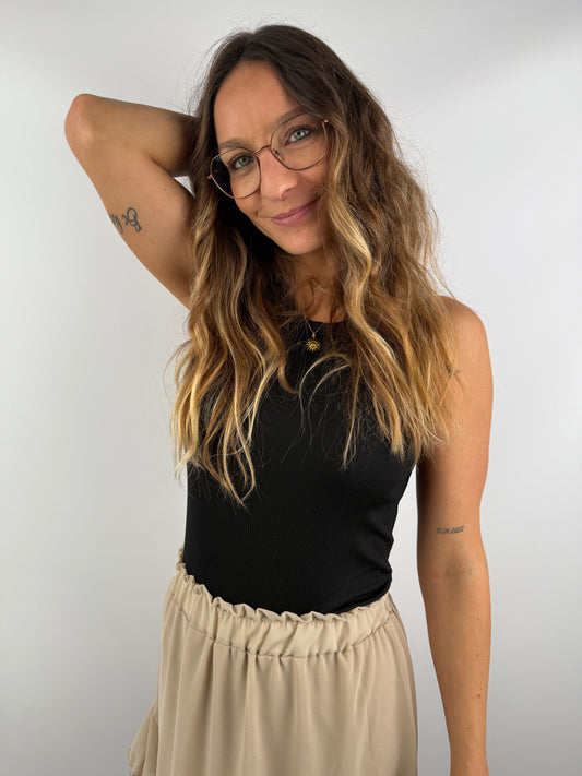 Frau mit schwarzem Ripp-Top und beigem Volant-Rock – natürlicher Look mit eleganter Schlichtheit.
