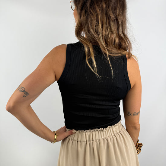 Rückenansicht eines Outfits mit schwarzem ärmellosen Top und beigem Rock mit Volant – klassisch und feminin kombiniert.
