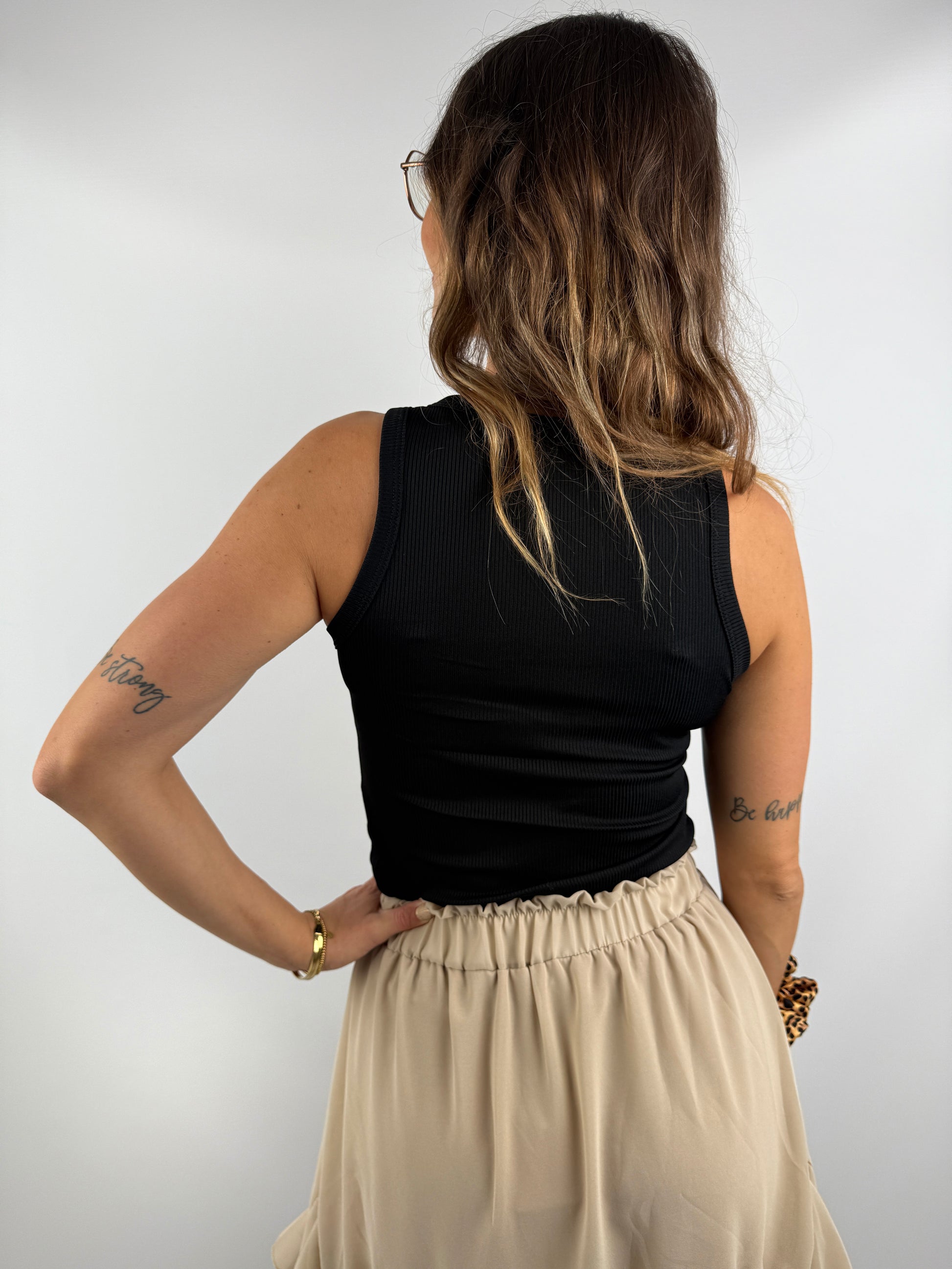Rückenansicht eines Outfits mit schwarzem ärmellosen Top und beigem Rock mit Volant – klassisch und feminin kombiniert.
