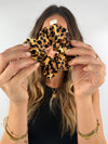 Frau hält einen Scrunchie aus echter Seide im Leo-Muster in die Kamera – luxuriöses Accessoire mit Glanz und Struktur.