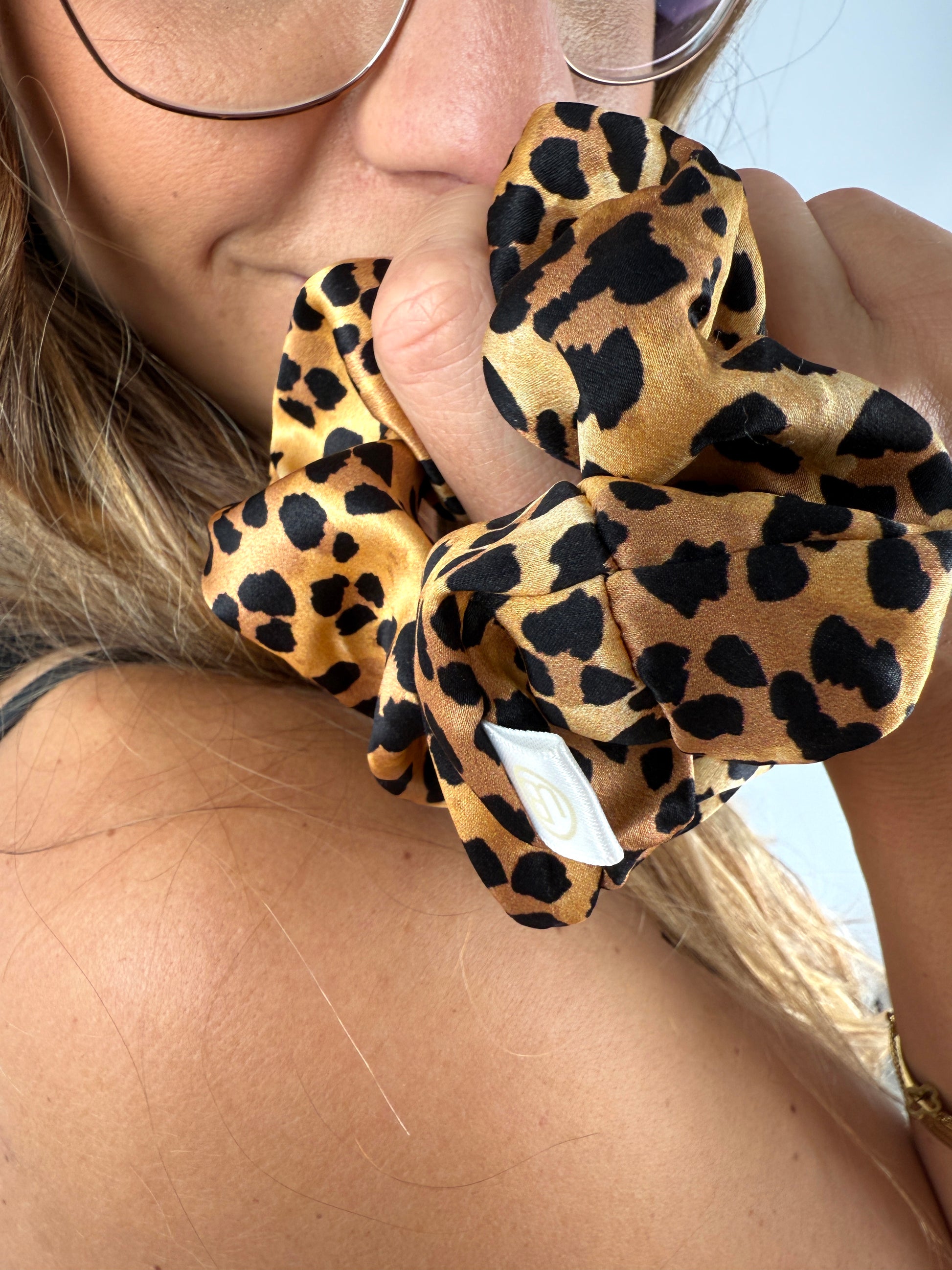 Nahaufnahme eines Seiden-Scrunchies im Leo-Print am Handgelenk – goldene Accessoires ergänzen den Look elegant.