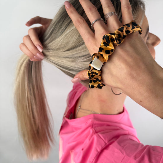 Frau bindet ihr Haar mit einem Seiden-Scrunchie im Leoparden-Design.