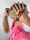 Frau bindet ihr Haar mit einem Seiden-Scrunchie im Leoparden-Design.