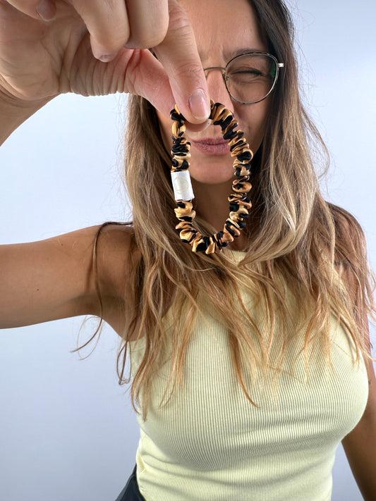Frau hält ein Scrunchie aus glänzender Seide mit Leopardenmuster in der Hand und lächelt – stilvolles Accessoire für Haare oder Handgelenk.