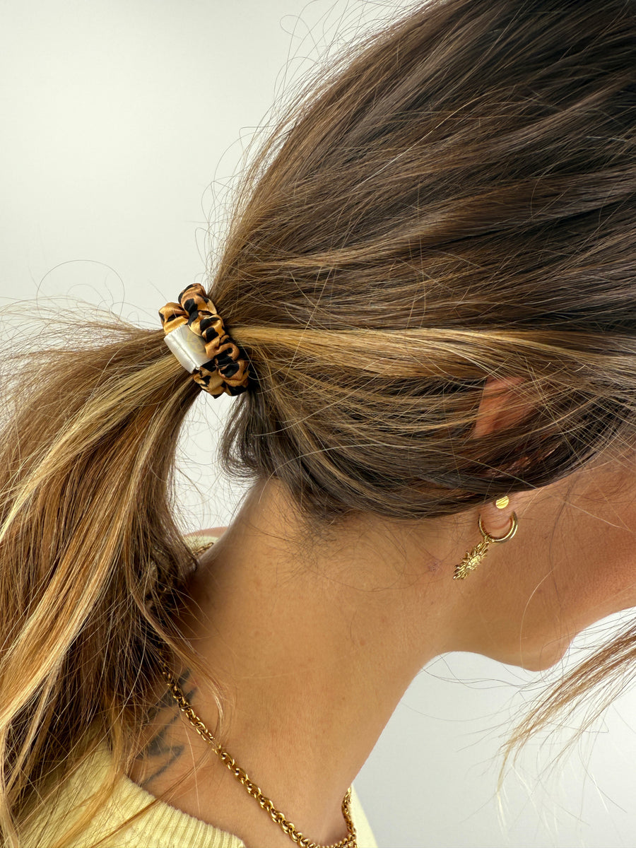 Nahaufnahme eines Seiden-Scrunchies im Haar, das edle Leopardenmuster wirkt luxuriös und trendig.