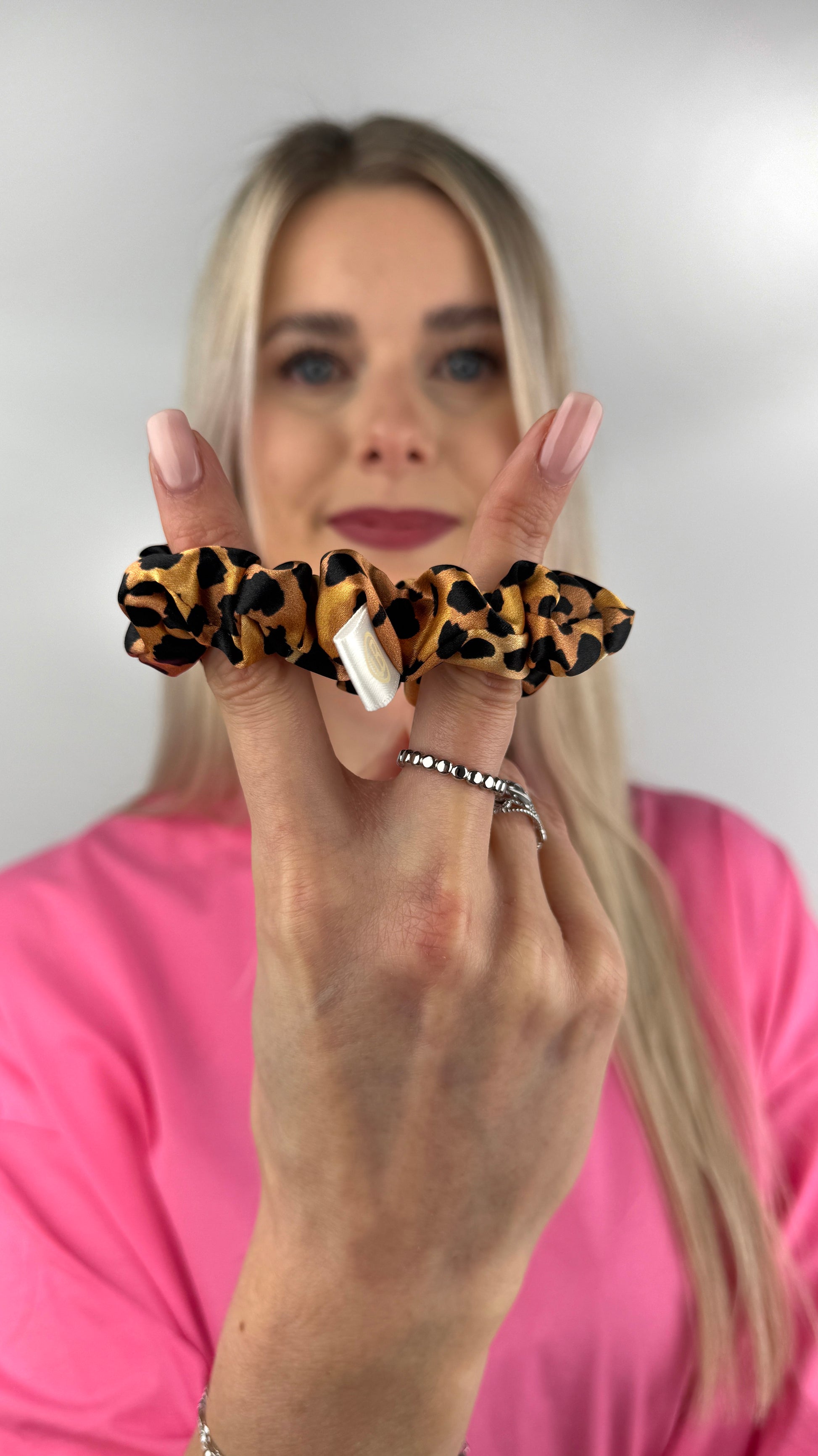 Frau hält ein Seiden-Scrunchie im Leopardenmuster in der Hand.