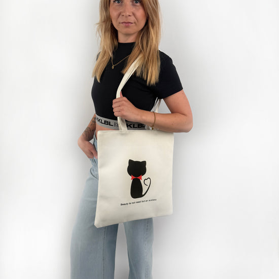 Weißer Stoffbeutel mit schwarzer Katze mit roter Schleife um den Hals auf der Vorderseite.