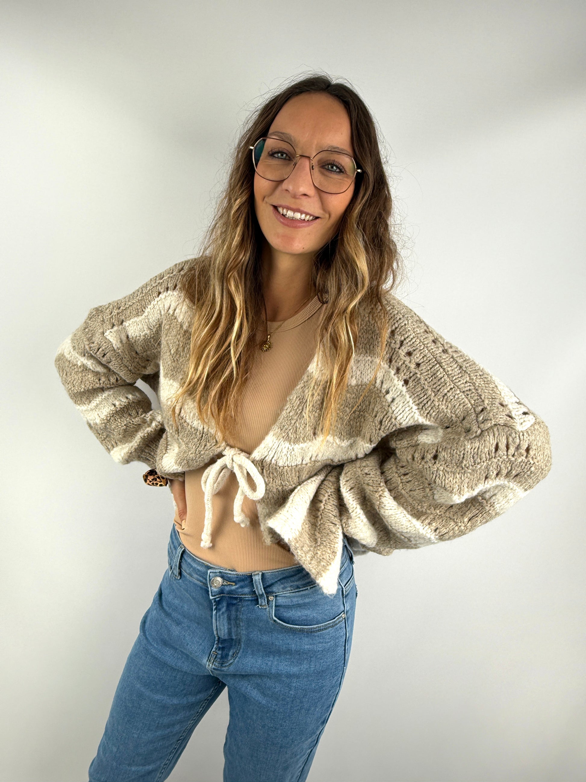 Frau trägt eine hellbeige Strickjacke mit Bindeschleife und lockeren Ärmeln – gemütlicher und lässig-schicker Look mit Jeans.