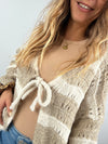 Detailaufnahme einer beige-creme gestreiften Strickjacke mit Schleife am Ausschnitt – kuscheliges Strickmaterial in harmonischen Naturtönen.