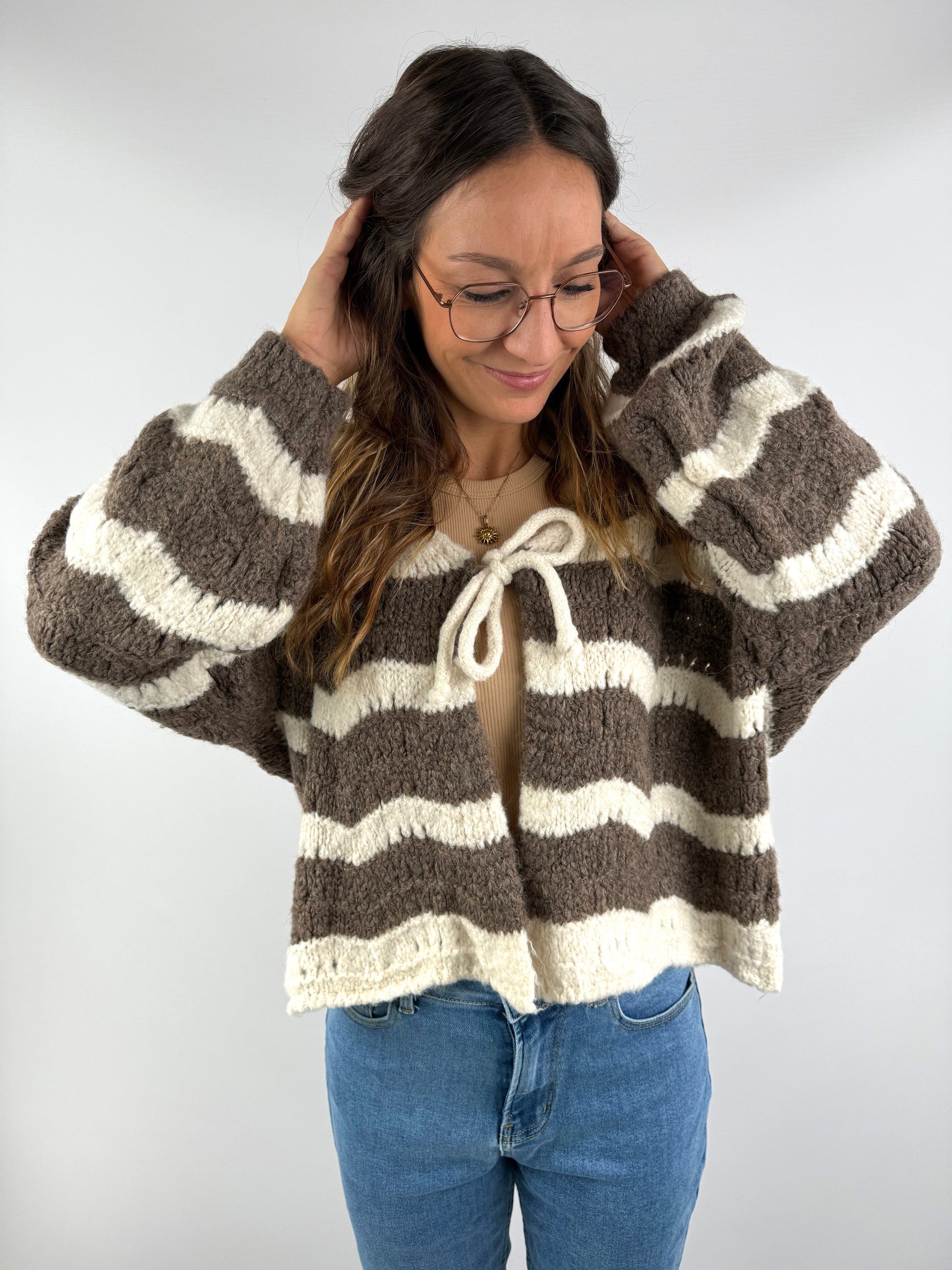 Braun-creme gestreifte Strickjacke mit Schleife vorne, kombiniert mit Jeans und beigem Top – lässig, weich und cozy gestylt.