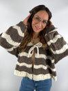 Frau trägt eine braun-cremefarbene Strickjacke mit breiten Streifen und Schleifendetail am Ausschnitt – kuscheliger, femininer Look.