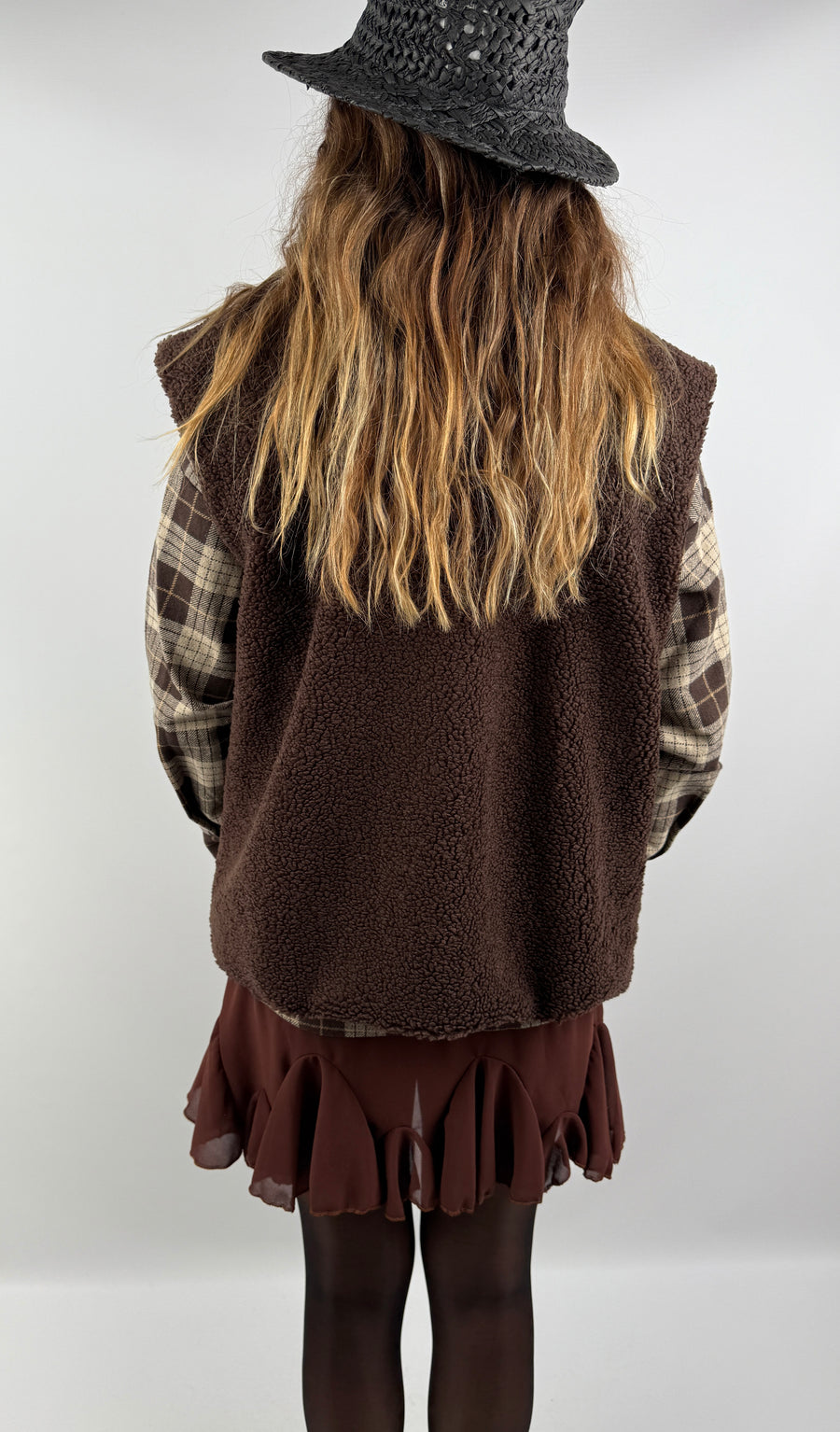 Rückenansicht einer braunen Teddyweste über kariertem Flanellhemd und Rock – gemütlicher und lässiger Herbststil.

