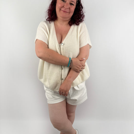 Wollweste in seichten farben mit kurzen Ärmeln und hellen größeren Knöpfen an der Vorderseite.