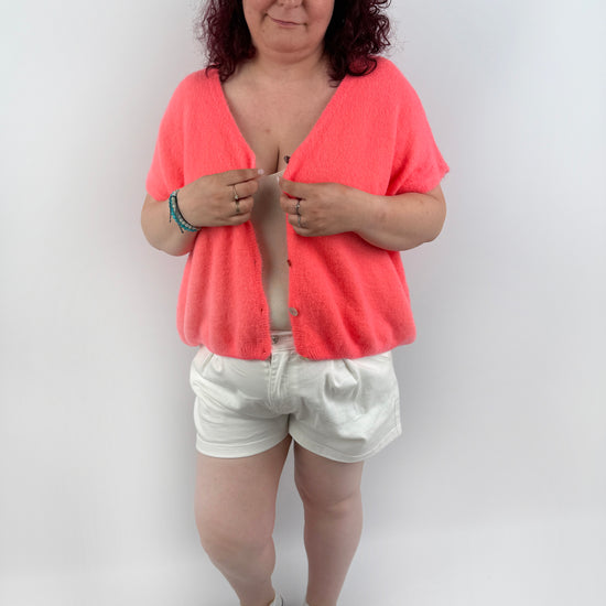 Wollweste in seichten farben mit kurzen Ärmeln und hellen größeren Knöpfen an der Vorderseite.