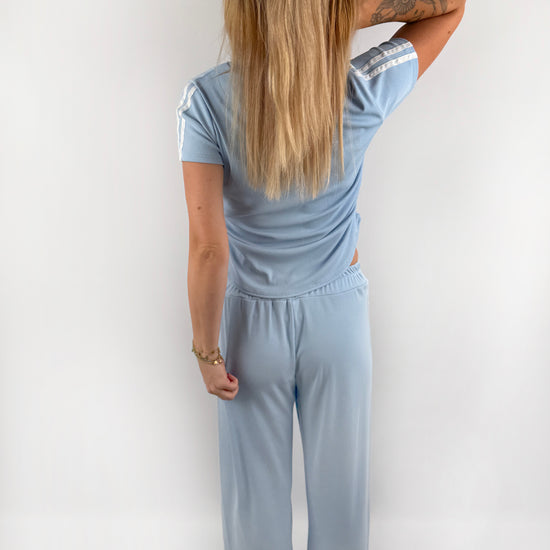 Zweiteiler bestehend aus Langer lockerer Hose und einem kürzeren T Shirt mit zwei weißen Streifen auf der Schulter in verschiedenen Farben.