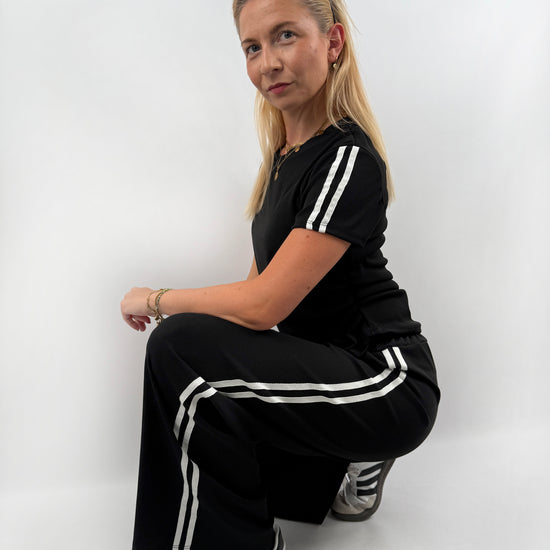 Zweiteiler bestehend aus Langer lockerer Hose und einem kürzeren T Shirt mit zwei weißen Streifen auf der Schulter in verschiedenen Farben.