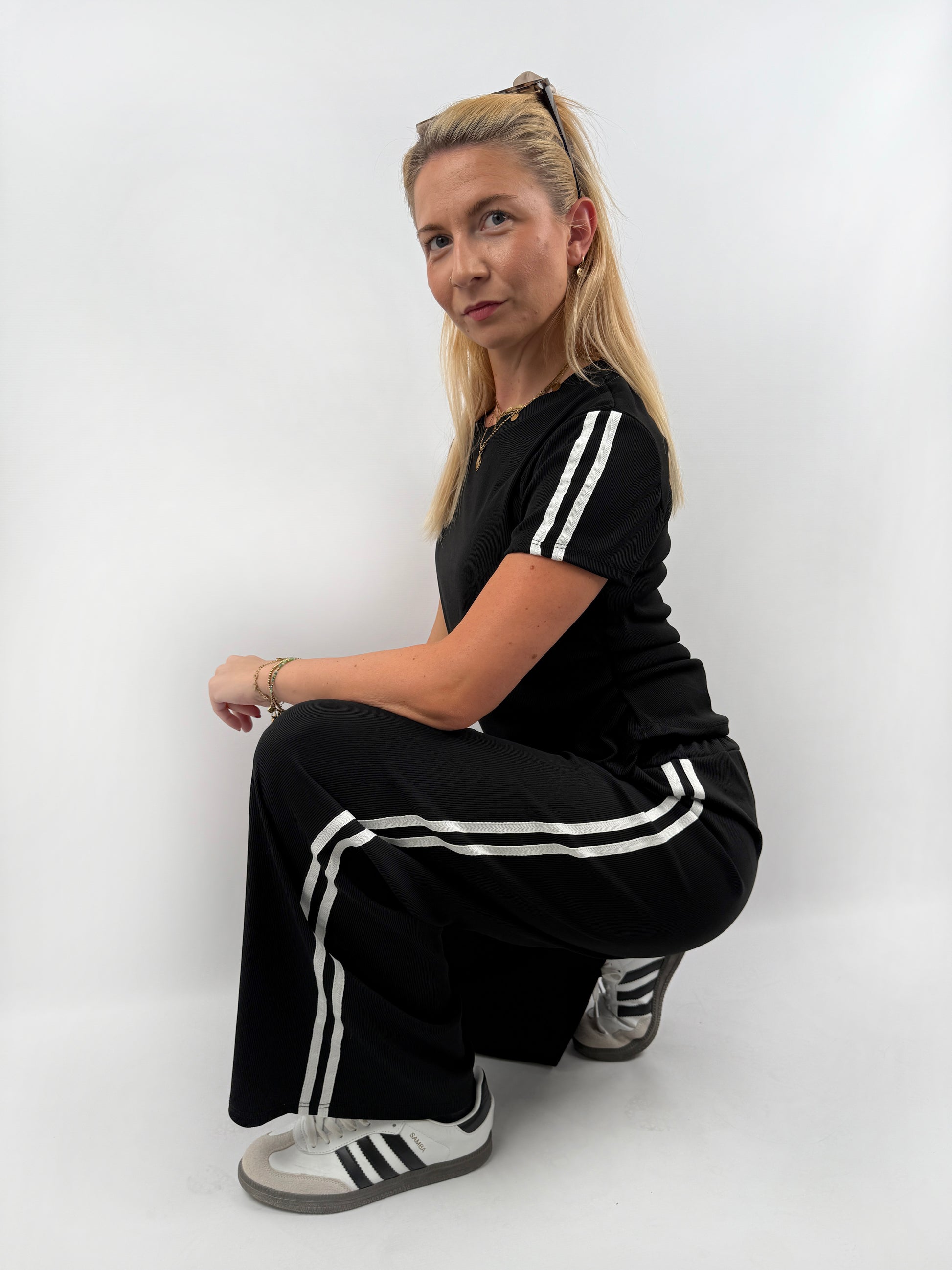 Zweiteiler bestehend aus Langer lockerer Hose und einem kürzeren T Shirt mit zwei weißen Streifen auf der Schulter in verschiedenen Farben.