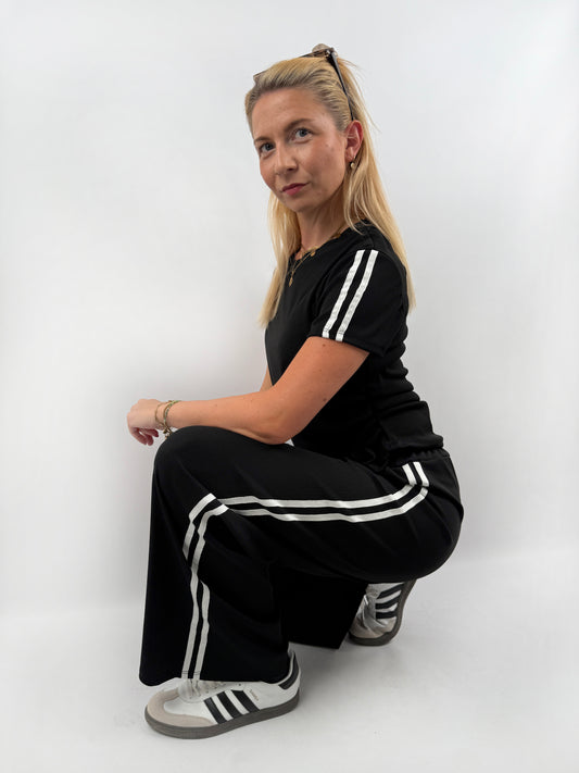 Zweiteiler bestehend aus Langer lockerer Hose und einem kürzeren T Shirt mit zwei weißen Streifen auf der Schulter in verschiedenen Farben.