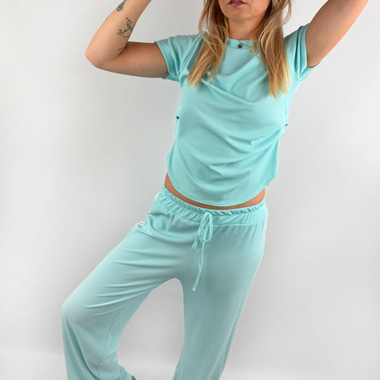 Zweiteiler bestehend aus Langer lockerer Hose und einem kürzeren T Shirt mit zwei weißen Streifen auf der Schulter in verschiedenen Farben.