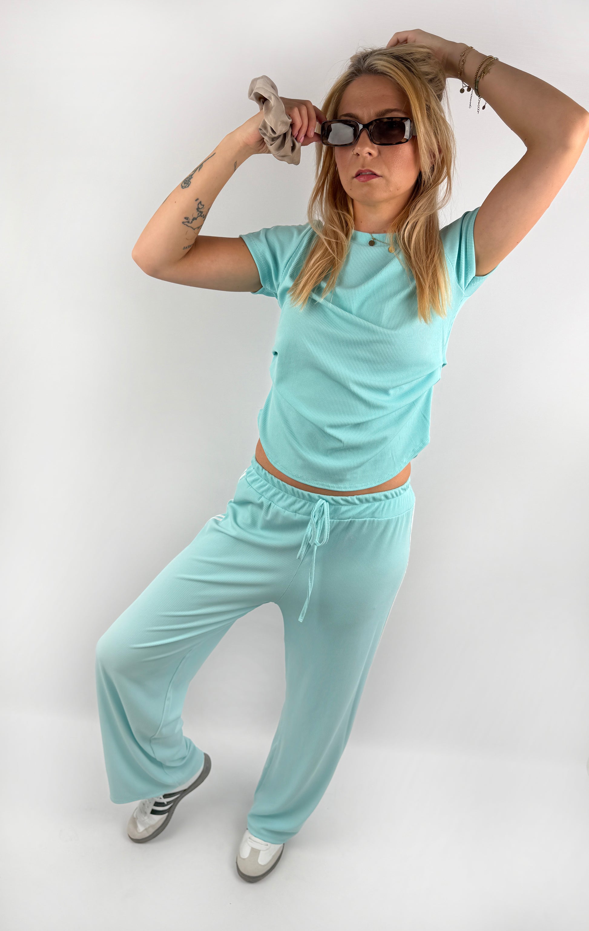 Zweiteiler bestehend aus Langer lockerer Hose und einem kürzeren T Shirt mit zwei weißen Streifen auf der Schulter in verschiedenen Farben.